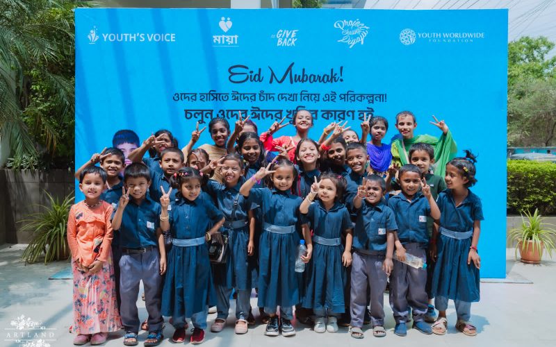 Children at a Youth Worldwide Foundation Eid event, in front of a backdrop carrying the Youth's Voice, Maya and Youth Worldwide Foundation logos